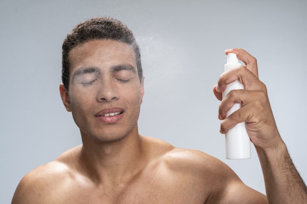 Handsome man spraying thermal water on his face