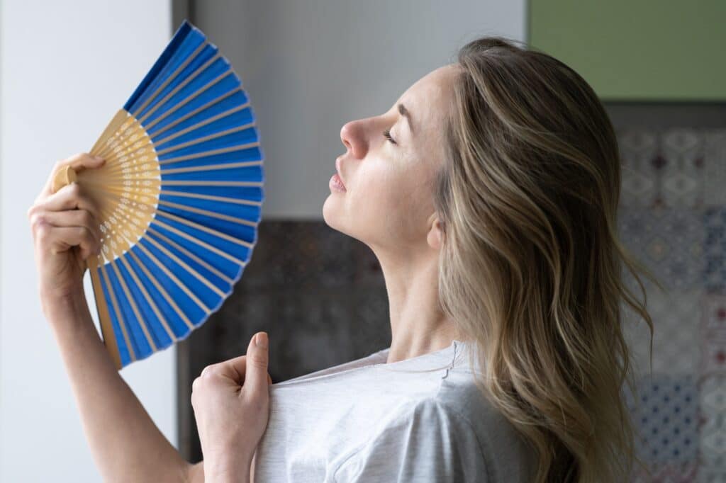Overheated woman in t-shirt using wave fan suffer from heat sweating, cools herself, feels sluggish