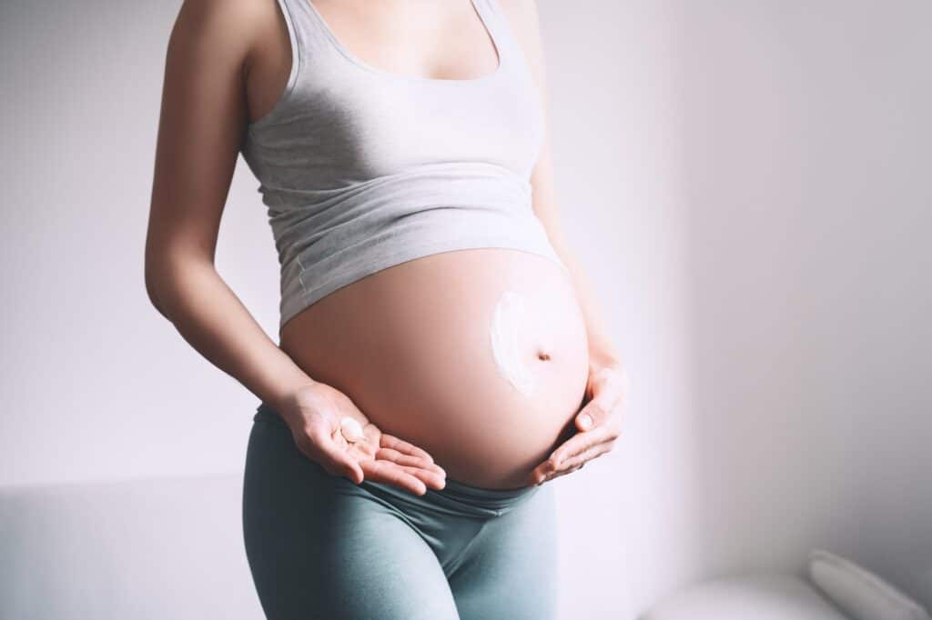 Pregnant woman applying moisturizer cream on her belly. Body skin care during pregnancy.