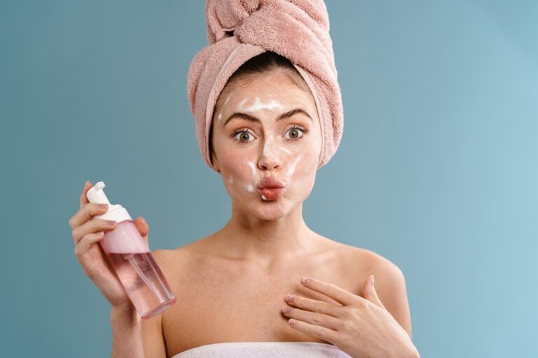 Surprised woman in towel cleaning her face with foam