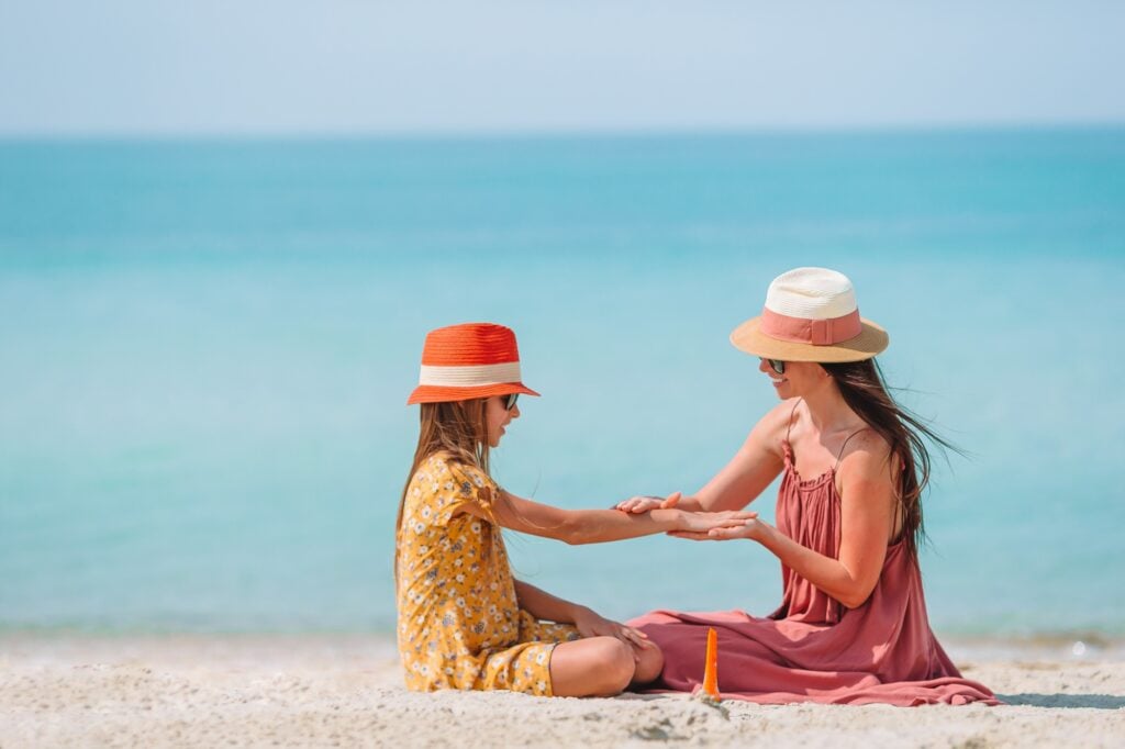 Young mother applying sun cream to daughter nose on the beach. Sun protection